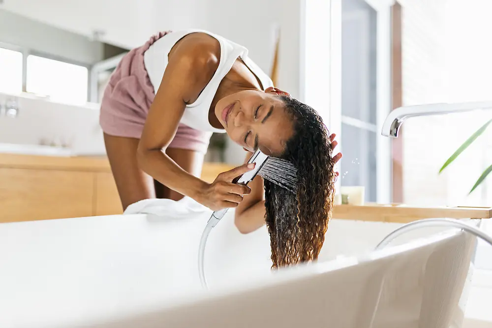 Frauen im Badezimmer waschen ihr braunes langes Haar in der Badewanne