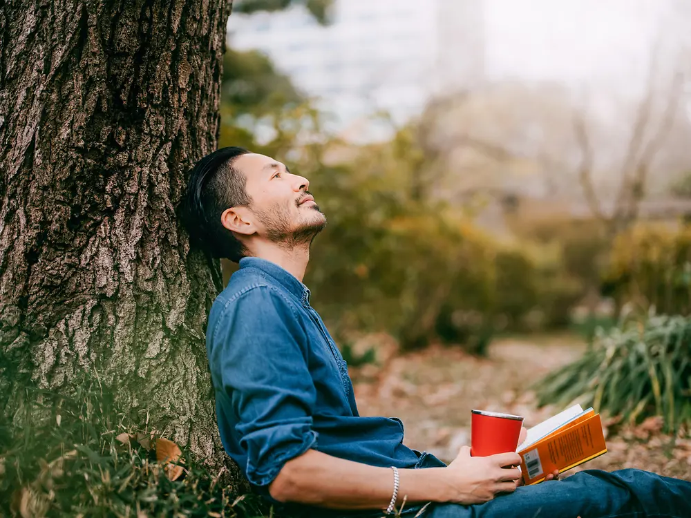 Ein Mann mit Buch lehnt an einem Baum